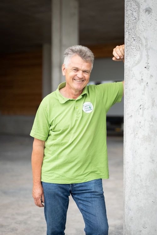 Älterer Mann mit grünem Poloshirt lehnt lächelnd an einer Betonwand