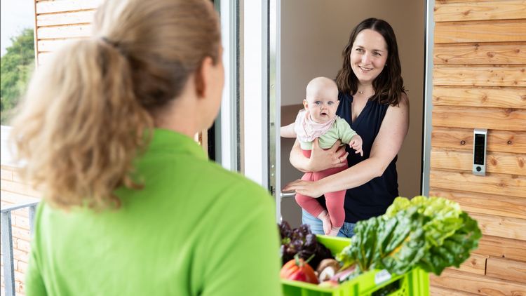 Frauenübergabe von Lebensmitteln an Mutter mit Baby an Holztür.