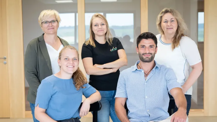 Fünf lächelnde Personen in einem hellen Büro, Gruppenfoto mit drei Frauen und einem Mann