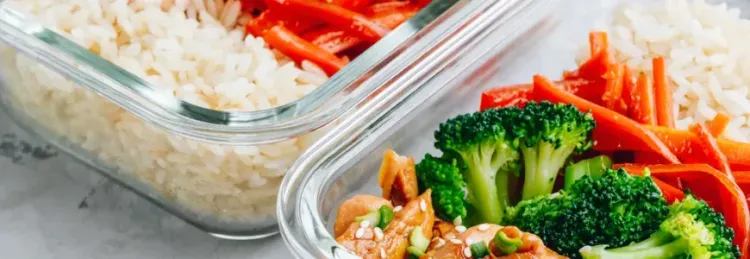 Glasbehälter mit Reis, Karotten, Brokkoli und Hühnchen mit Sesam und Frühlingszwiebeln