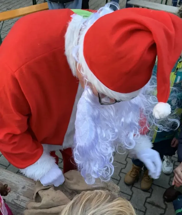 Weihnachtsmann mit rotem Anzug und weißem Bart verteilt Geschenke an Kinder im Freien