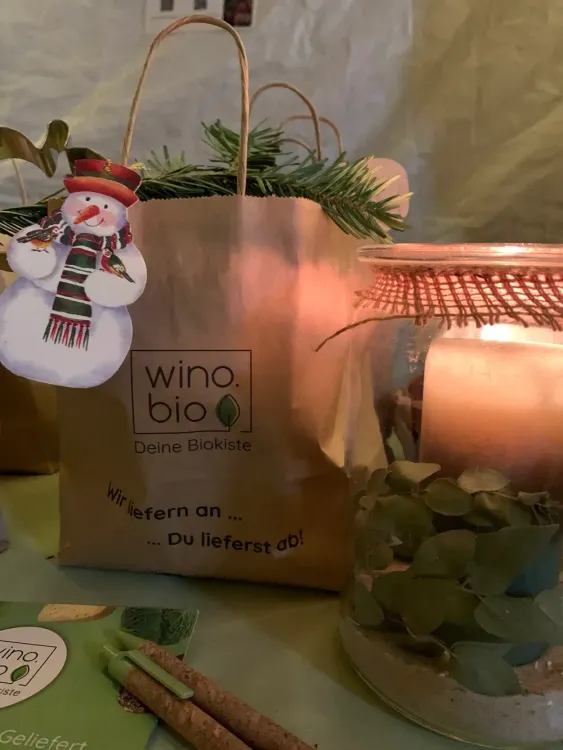 Weihnachtliche Papiertüte mit Tannenzweigen und Schneemannanhänger neben Kerze in Glas mit Blättern