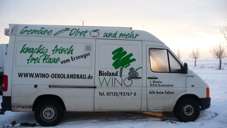 Weißes Lieferfahrzeug mit Werbung für Bioland Gemüse und Obst vor verschneiter Landschaft bei Sonnenuntergang
