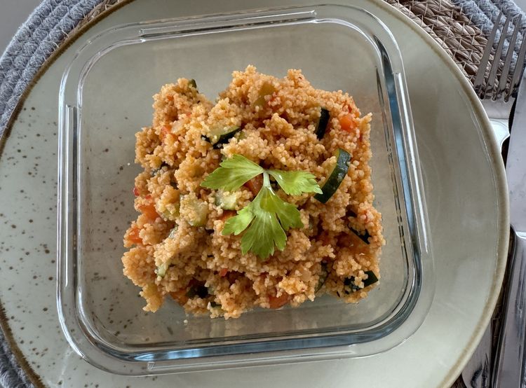 Glasbehälter mit Couscous und Gemüse, garniert mit Petersilie auf einem Teller serviert.