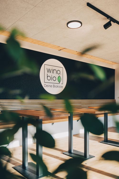 Moderner Innenraum mit Holzsitzen und Tischen vor Wand mit Logo von wino.bio Deine Biokiste
