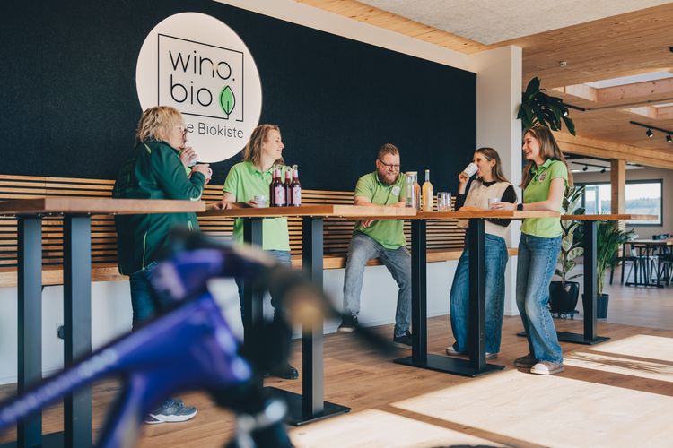 Menschen in grünen Shirts treffen sich an einem Tisch in einem modernen Büro mit wino.bio Logo an der Wand