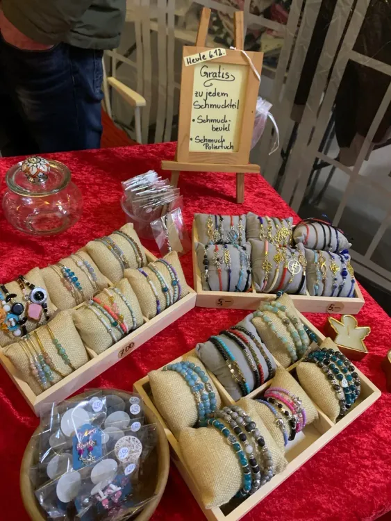 Schmuckstand mit bunten Armbändern auf Kissen und Schild mit Gratis Schmuckbeutel und Poliertuch.