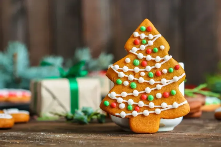 Weihnachtsbaumförmiger Lebkuchen mit bunter Zuckerdekoration vor Geschenken auf Holztisch