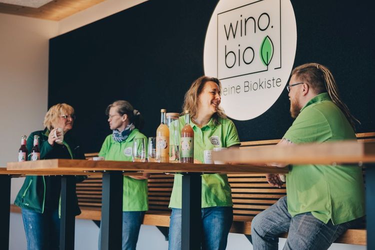 Vier Personen in grünen Hemden unterhalten sich an einem Holztisch neben dem Logo von wino.bio.