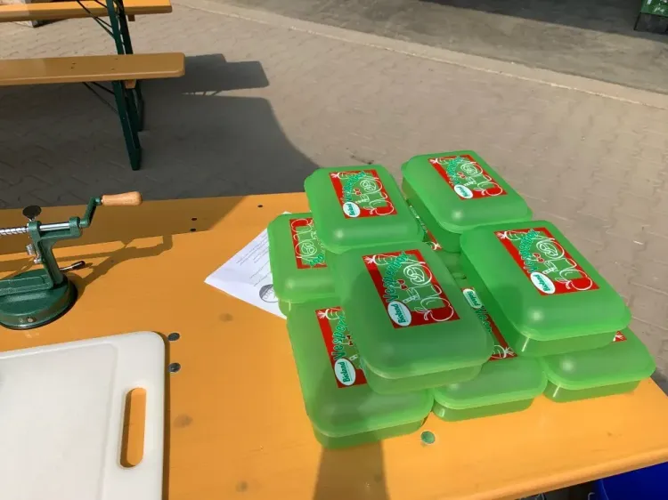 Grüne Plastikbehälter stapeln sich auf einem Holztisch neben einem Handkurbelgerät im Freien.
