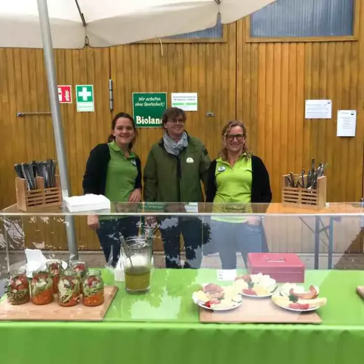 Drei Frauen hinter einem Marktstand mit grünen Tischdecken und regionalen Bioprodukten