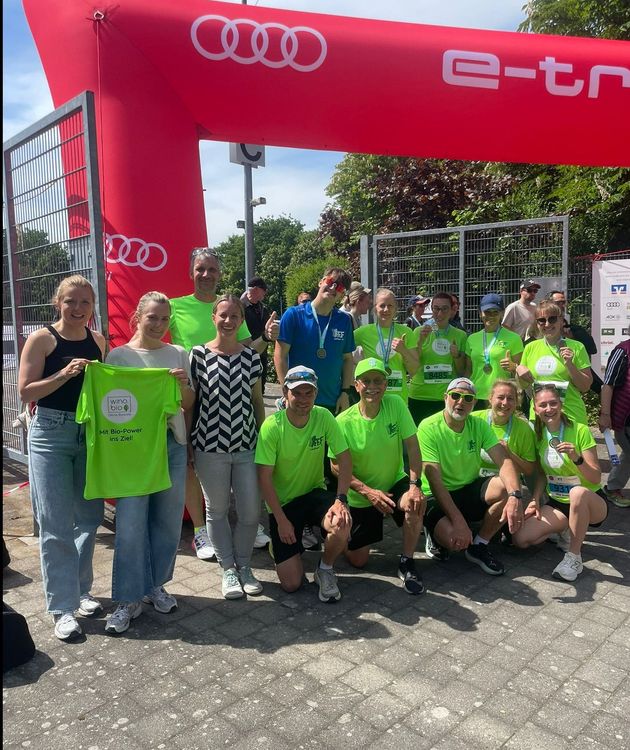 Gruppenfoto von Läufern in neongrünen Trikots unter rotem Audi e-tron Torbogen nach Laufveranstaltung