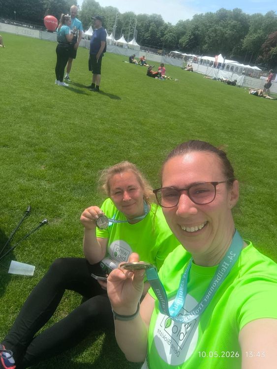 Zwei Frauen in grünen Shirts zeigen stolz ihre Medaillen auf einer Wiese nach sportlicher Veranstaltung