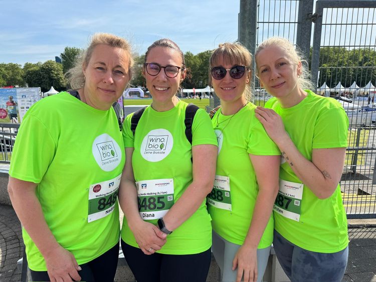 Vier Frauen in neongrünen T-Shirts mit Laufnummern bei einer Outdoor-Veranstaltung, lachend und nah beieinander
