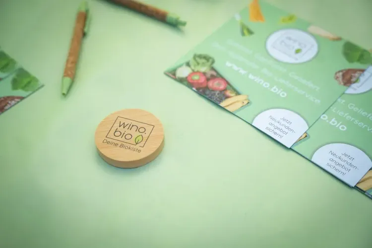 Rundes Holzobjekt mit Logo von wino.bio und grüne Werbeflyer auf grünem Untergrund
