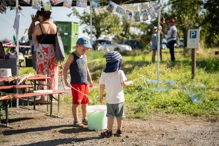 Zwei Kinder machen große Seifenblasen auf einem sonnigen Markt mit Besuchern im Hintergrund