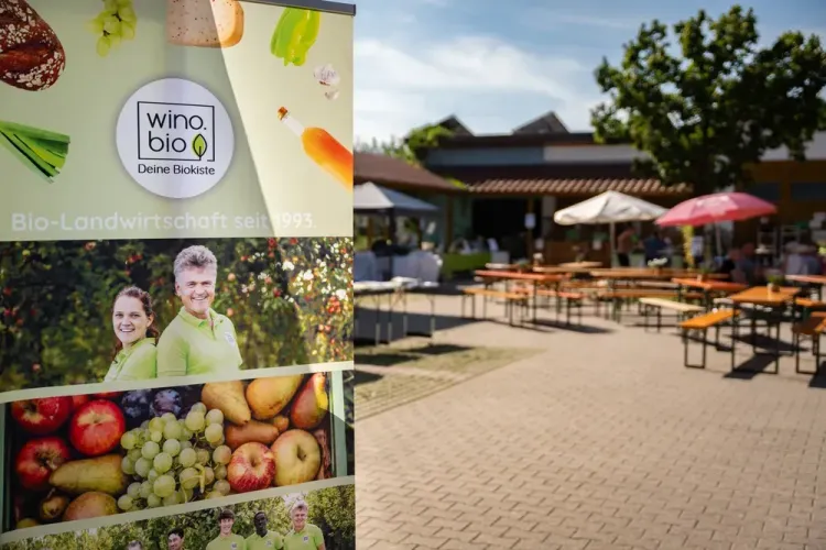 Werbebanner von wino.bio neben einem sonnigen Außenbereich mit Biergartenbänken und Sonnenschirmen