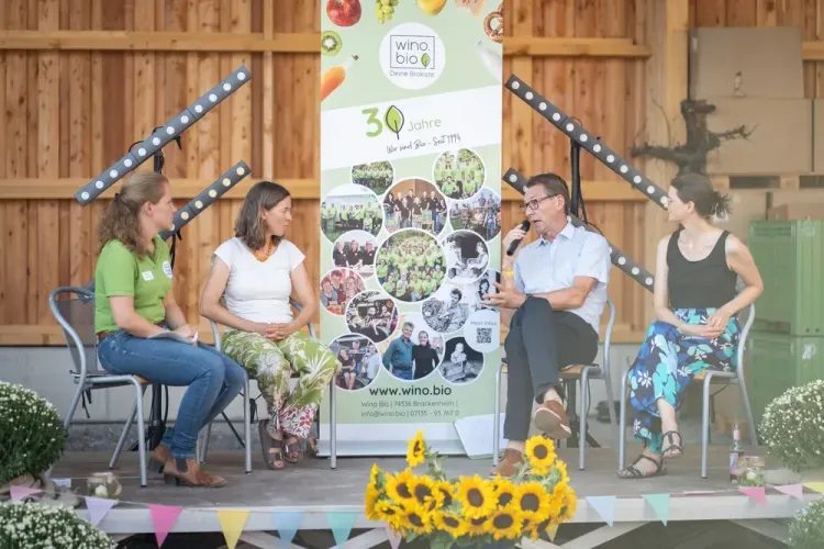 Podiumsdiskussion mit vier Personen vor einem Banner von Wino Bio mit Sonnenblumen im Vordergrund