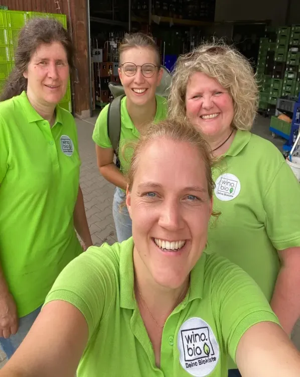 Vier lächelnde Frauen in grünen Poloshirts mit wino.bio Logos im Lager