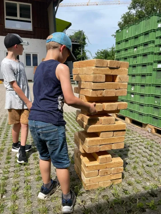Zwei Jungen spielen draußen mit einem übergroßen Jenga-Turm aus Holzklötzen