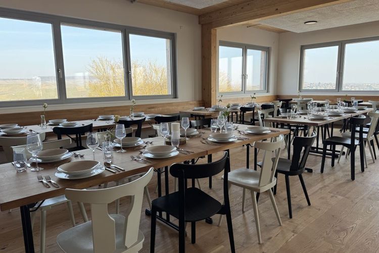 Esszimmer mit langen Holztischen, geschmückten Tellern und Gläsern vor großen Fenstern mit Blick auf Landschaft
