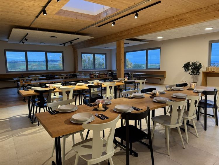 Moderner Speiseraum mit Holztischen, schwarz-weißen Stühlen und Fensterblick auf Landschaft.