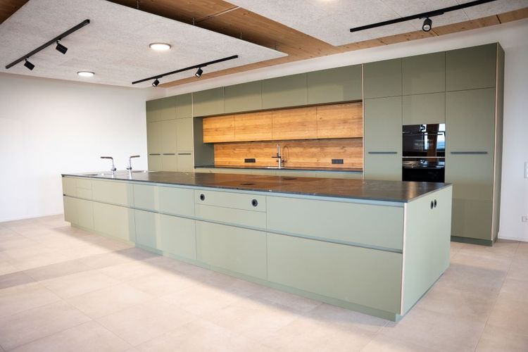 Moderne grüne Küche mit großer Insel und Holzrückwand in hellem Raum