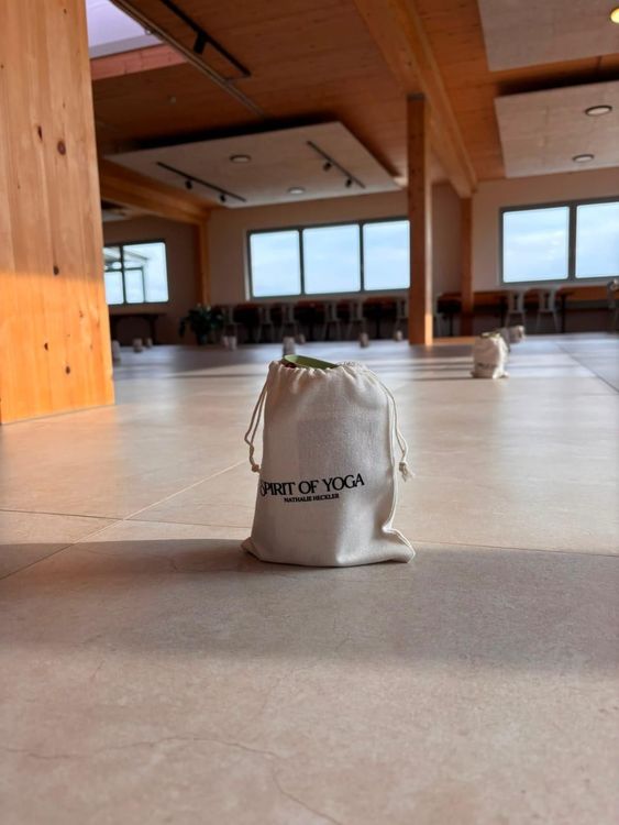 Beutel mit Schriftzug Spirit of Yoga steht in hellem Yogaraum mit Holzbalken und großen Fenstern