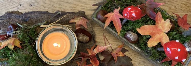 Herbstliche Dekoration mit brennender Kerze, bunten Blättern, Moos, Kastanien und Deko-Fliegenpilzen auf Holzuntergrund