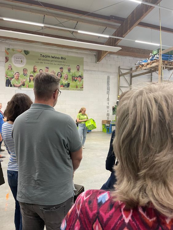 Menschen stehen in Lagerhalle vor Team-Wino-Bio-Plakat mit grünen T-Shirts