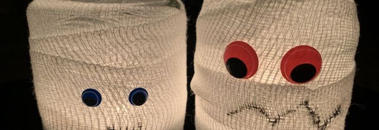 Zwei Halloween-Kerzen mit weißen Mullbinden und großen bunten Augen auf dunklem Hintergrund