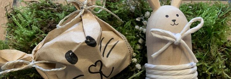 Zwei handgemachte Osterdekorationen aus Holz und Papier liegen auf Moos, beide mit Hasenmotiven verziert.