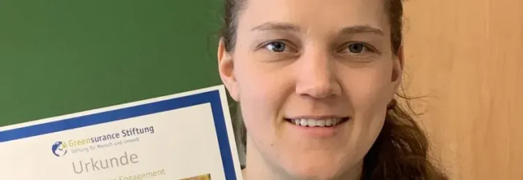 Frau hält eine Urkunde der Greensurance Stiftung vor grünem Hintergrund