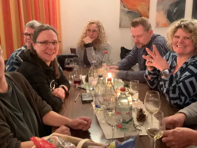 Menschen sitzen gemeinsam an einem Tisch mit Kerzen, Getränken und unterhalten sich fröhlich