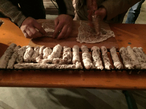 Personen rollen traditionelle deutsche Wurst auf Holzbrett, viele Würste liegen auf einem Rost