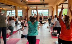 Gruppe von Menschen praktiziert Yoga in einem hellen Raum mit großen Fenstern und Holzdecke
