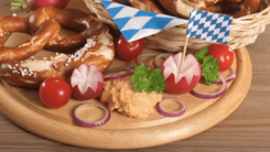 Bayerische Brezeln mit Radieschen, Tomaten, Zwiebeln und Obazda auf Holzbrett mit blau-weißem Fähnchen