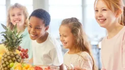 Vier lachende Kinder stehen zusammen an einem Tisch mit frischem Obst.