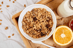 Schale mit Müsli, daneben Orangenscheibe und Milchflasche auf Holztisch